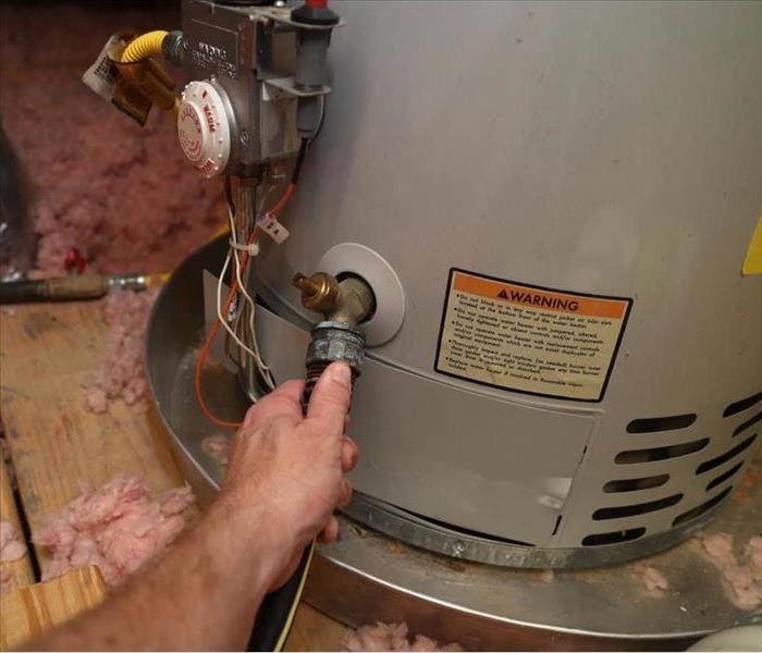 Hand connects the hose to a domestic water heater to perform maintenance.