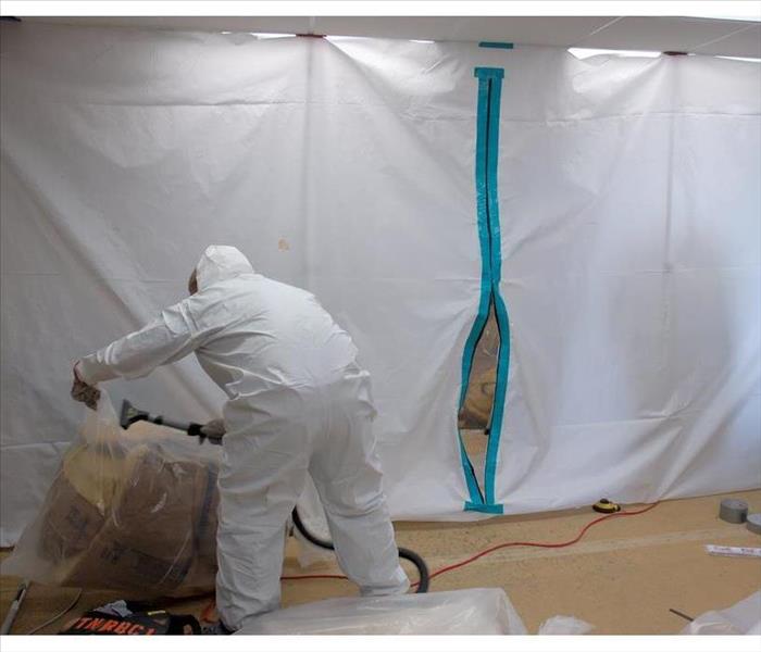 Person wearing protective gear while putting plastic barriers in a home (mold containment)